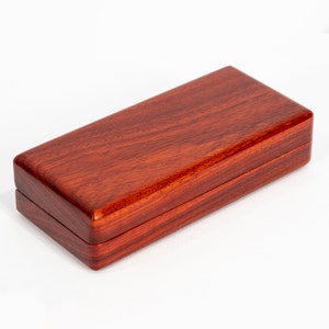 May include: A rectangular wooden box with a rich reddish-brown color. The box has a smooth, polished finish and is made of a fine-grained wood.
