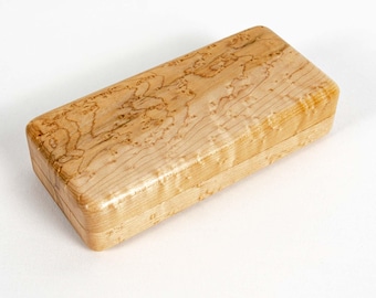 May include: A rectangular wooden box with a smooth, polished finish. The light-colored wood features a distinct, swirling grain pattern with natural tan and cream-colored markings throughout the surface, showcasing the organic texture of the material.
