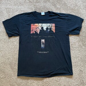 May include: Black t-shirt with a graphic of a movie poster for "Night of the Comet". The poster features a silhouette of people standing in front of a doorway with a comet in the background. The text "It was like the last thing on earth. They never expected it." is printed below the graphic.