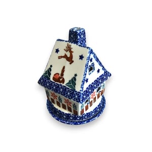 Könnte beinhalten: Ein blauer und weißer Keramik-Räucherofen in Form eines Hauses mit einem Hirsch- und Hasendesign. Das Haus hat einen Schornstein und eine Basis mit braunem und rotem Rand.