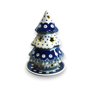 Peut inclure: Un photophore en forme de sapin de Noël en céramique. L'arbre est blanc avec des motifs floraux bleus et des découpes en forme d'étoiles. La base est une assiette assortie bleue et blanche. L'arbre mesure environ 15 cm de haut.