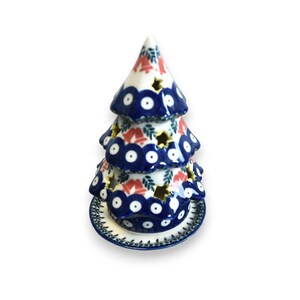 May include: A blue and white ceramic Christmas tree candle holder with red and green accents. The tree is tiered and has a base.