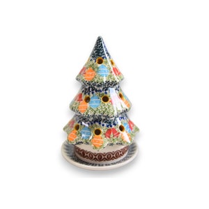 Op de afbeelding: Een kerstboom-ornamentenhouder van keramiek met een witte basis en een groene, blauwe en rode boom met kleurrijke ornamenten. De boom heeft gaten voor kaarsen of theelichtjes.