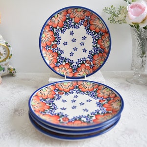 Könnte beinhalten: Set aus vier Keramiktellern mit Blumenmuster. Die Teller haben einen weißen Hintergrund mit einem blauen und orangefarbenen Blumenmuster. Die Teller sind übereinander gestapelt.