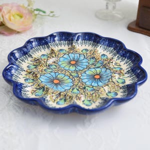 May include: A ceramic, scalloped-edge plate with a blue floral design. The plate features a dark blue rim and a cream-colored interior with blue and orange flowers. The plate is likely used for serving food.