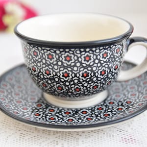 May include: A black and white teacup and saucer set with a red floral pattern. The cup has a handle and the saucer is round.