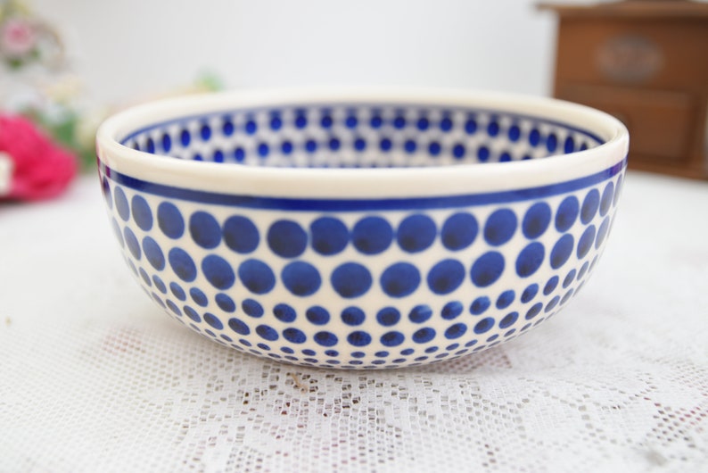 May include: A white ceramic bowl with a blue polka dot pattern. The bowl is round and has a wide rim.