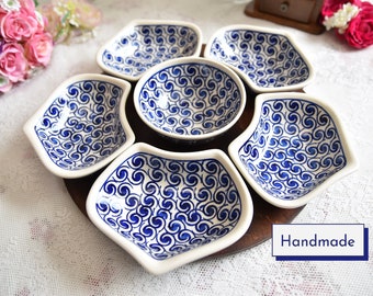 May include: A set of six white ceramic bowls with a blue swirl pattern. The bowls are arranged in a circle on a wooden base. The bowls are handmade.