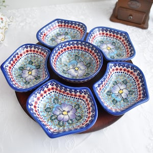 Könnte beinhalten: Ein Set aus sechs blauen und weißen Keramik-Schalen mit Blumendesigns. Die Schalen sind in einem Kreis auf einem Holzsockel angeordnet.