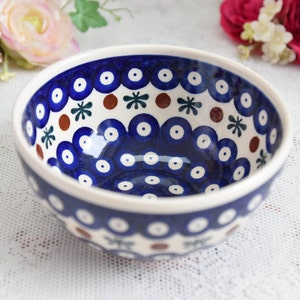 Peut inclure: Un bol en céramique bleu et blanc avec un motif décoratif de cercles, de points et de fleurs. Le bol a une bordure brune et est parfait pour servir des en-cas ou des salades.