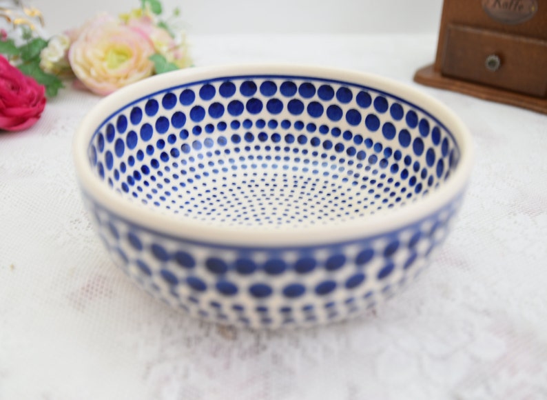 May include: A white ceramic bowl with a blue polka dot pattern. The bowl is round and has a slight lip around the edge.
