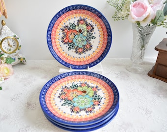 Puede incluir: Juego de cuatro platos de cena de cerámica azul y blanca con un diseño floral con flores rosas, naranjas, amarillas y verdes. Los platos tienen un borde decorativo con un patrón repetitivo.