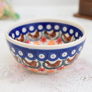 May include: A small, blue and white ceramic bowl with a floral and bird design. The bowl has a white interior and a blue rim.