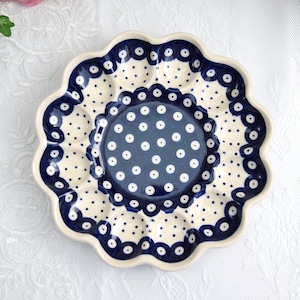 May include: A ceramic serving dish with a scalloped edge and a central, smaller dish. The dish features a cream-colored base with blue polka dots and a blue border. The center dish is blue with white polka dots.