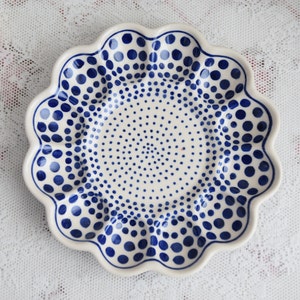 Op de afbeelding: Een wit keramiek bord met een blauw stippenpatroon. Het bord heeft een gegolfde rand en is perfect om snacks of desserts op te serveren.