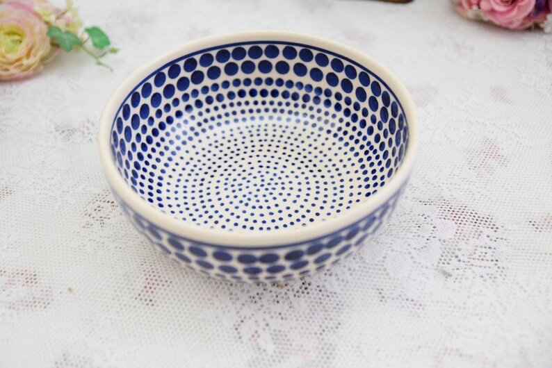 May include: A white ceramic bowl with a blue polka dot pattern. The bowl is round and has a wide rim.