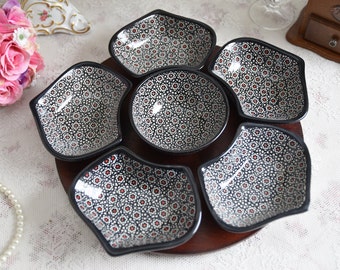 May include: A wooden serving tray with six black and white ceramic bowls with a red floral pattern. The bowls are arranged in a flower shape.