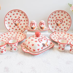 May include: A set of red and white heart patterned ceramic dishes, including two egg cups, two salt and pepper shakers, a butter dish, and four plates.