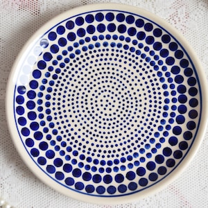 May include: A white ceramic plate with a blue and white polka dot pattern. The dots are arranged in a spiral pattern, getting larger as they move away from the centre of the plate.