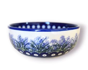 May include: A small white ceramic bowl with a blue rim and a floral design. The bowl features a border of blue and white dots and a floral pattern of purple flowers and green leaves.