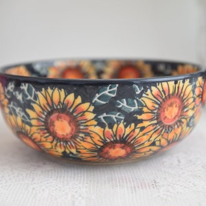 Könnte beinhalten: Eine Keramikschüssel mit schwarzem Hintergrund und einem Sonnenblumenmuster in Gelb-, Orange- und Rottönen.