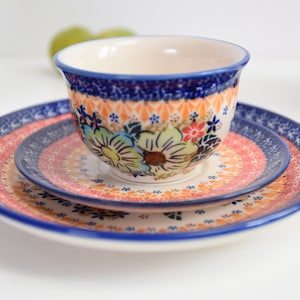 May include: A set of three ceramic plates with a floral design in shades of blue, pink, and green. The plates are nested together, with the smallest plate on top. The plates have a white background with a blue border.