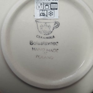 May include: White ceramic saucer with black text that reads "USING IN:" and includes icons for microwave, oven, dishwasher, and freezer safe. The saucer also has black text that reads "CERAMIKA Boleslawiec HAND MADE IN POLAND".