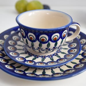 May include: A blue and white ceramic teacup and saucer set with a peacock feather design. The set features a white background with blue and brown accents.