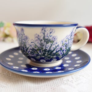 May include: A blue and white teacup and saucer set with a floral pattern. The cup has a white background with a blue rim and a floral design in shades of purple and green. The saucer has a blue background with white polka dots.