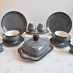 Puede incluir: Un juego de platos de cerámica azul y blanco con un patrón floral. El juego incluye dos tazas de té y platillos, dos hueveras, una mantequillera y dos saleros y pimenteros.