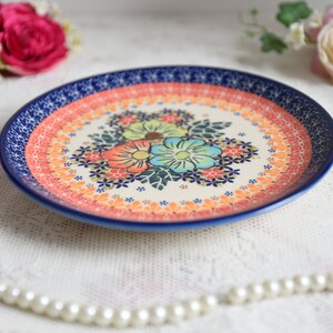 May include: A blue and white ceramic plate with a floral design. The plate has a red, orange, and yellow border. The flowers are pink, blue, and green.
