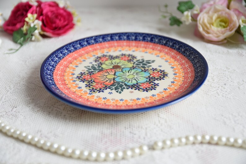 May include: A blue and white ceramic plate with a floral design. The plate has a red, orange, and yellow border. The flowers are pink, blue, and green.