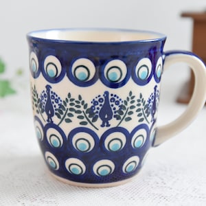 May include: A blue and white ceramic mug with a peacock design. The mug has a rounded body and a handle.