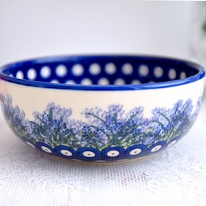 May include: A white ceramic bowl with a blue and white floral pattern. The bowl has a blue rim with white polka dots.