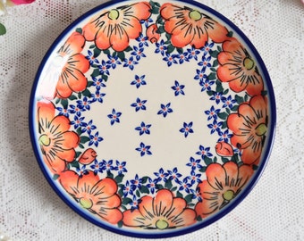 Puede incluir: Un plato de cerámica blanco con un borde azul y un diseño floral. El diseño presenta flores naranjas con hojas verdes y flores azules.