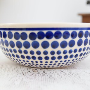 May include: A white ceramic bowl with a blue polka dot pattern. The dots are arranged in a graduated pattern, getting smaller as they go down the bowl.