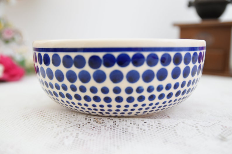 May include: A white ceramic bowl with a blue polka dot pattern. The dots are arranged in a graduated pattern, getting smaller as they go down the bowl.