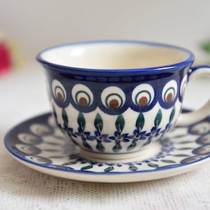 May include: A blue and white ceramic teacup and saucer set with a peacock feather design. The cup and saucer have a white background with blue and green accents.