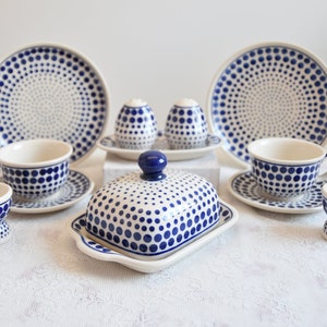 Könnte beinhalten: Ein Set aus blau-weißen Keramikgeschirr mit Punkten, bestehend aus zwei Teetassen und Untertassen, zwei Eierbechern, einer Butterdose und zwei Salz- und Pfefferstreuern.