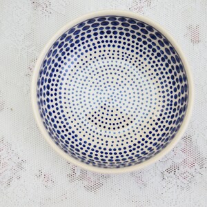 May include: A white ceramic bowl with a blue polka dot pattern. The dots are arranged in a concentric circle pattern.