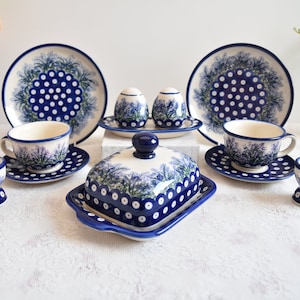 Könnte beinhalten: Ein blaues und weißes Keramik-Tee-Set mit einem Blumenmuster. Das Set enthält zwei Teetassen und Untertassen, eine Butterdose, zwei Eierbecher und zwei Salz- und Pfefferstreuer.