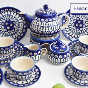 May include: A handmade tea set with a blue and green peacock design. The set includes a teapot, creamer, sugar bowl, and four teacups and saucers.