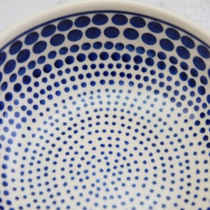 May include: A white ceramic bowl with a blue polka dot pattern. The dots are arranged in a graduated pattern, with larger dots at the top and smaller dots at the bottom.
