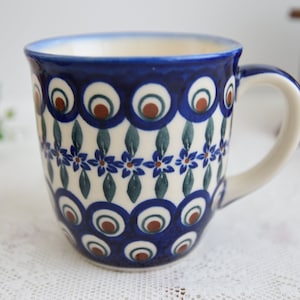 Puede incluir: Una taza de cerámica azul y blanca con un diseño de pluma de pavo real. La taza tiene un asa y está decorada con colores azul, blanco y marrón.