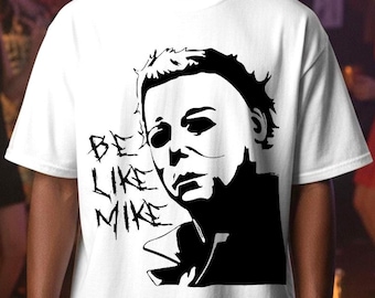 Może przedstawiać: Biała koszulka z czarno-białą grafiką twarzy postaci i napisem "BE LIKE MIKE". Projekt jest stylizowaną ilustracją. Koszulka ma okrągły dekolt i krótkie rękawy.