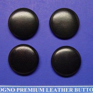 May include: Four black leather buttons with a textured surface.  The buttons are round and have a diameter of approximately 1 inch.