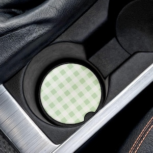 May include: A car cup holder with a green and white checkered coaster. The coaster is round and fits snugly in the cup holder. The car's interior features black leather and silver trim.