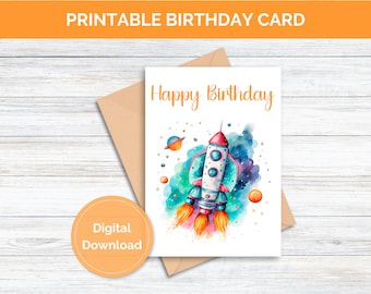 May include: Printable birthday card featuring a watercolor illustration of a rocket ship flying through space with planets and stars. The card says "Happy Birthday" at the top.