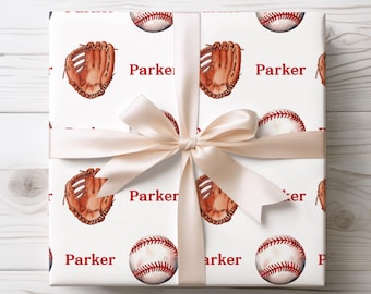May include: White gift wrap featuring a repeating pattern of baseballs and mitts in brown and red. The name "Parker" is printed in red. A cream-colored satin ribbon is tied around the gift.