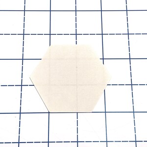 K&ouml;nnte beinhalten: Eine leere, cremefarbene, sechseckige Papierform, die sich auf einer wei&szlig;en Oberfl&auml;che mit einem blauen Rastermuster befindet. Das Raster besteht aus durchgezogenen und gestrichelten Linien.